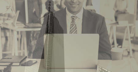 Composition of smiling businessman using laptop over modern office building. global business and...