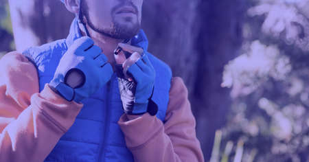 Composition of caucasian man putting helmet on bicycle in forest. sport, fitness and active lifestyle concept digitally generated image.の写真素材