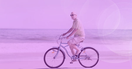 Composition of senior man riding bicycle on beach by sea with purple tint. holiday, sport, fitness...