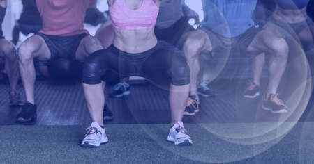 Composition of low section of fit people doing squats in gym with spots of light. sport, fitness and active lifestyle concept digitally generated image.の写真素材