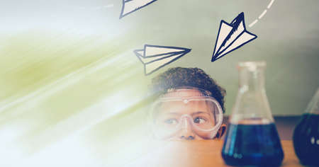 Composition of paper planes over schoolboy in protective glasses in school laboratory. science, learning and knowledge concept digitally generated image.の写真素材