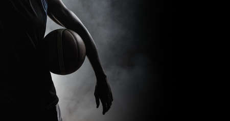 Composition of athletic male basketball player over smoke on black background. sport, fitness and active lifestyle concept digitally generated image.の写真素材