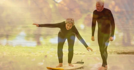 Composition of senior couple with surfboard on beach and autumn foliage. healthy active retirement...