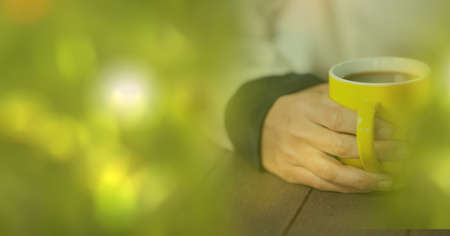 Composition of woman holding yellow cup of coffee over wooden surface with copy space. drink and caffeine concept digitally generated image.の写真素材