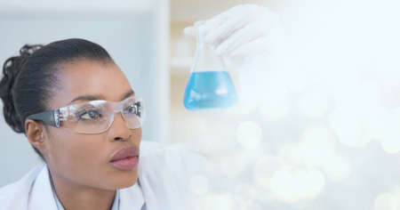 Composition of female lab technician holding conical flask, with white bokeh copy space to right....