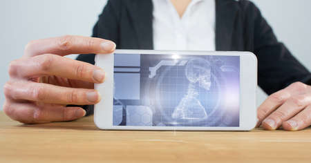 Composition of woman at desk holding smartphone with screen showing scientific research interface. global medicine, research and digital interface concept digitally generated image.の写真素材