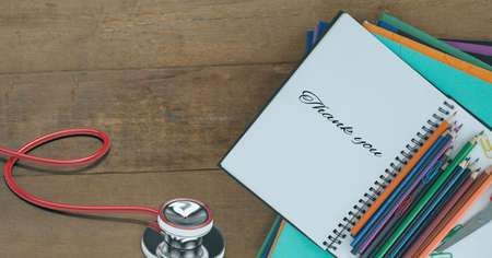 Composition of notebook with thank you note, with stethoscope, stationery and pencils on wooden...