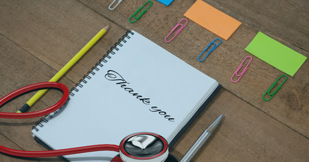 Composition of notebook with thank you note, with stethoscope and stationery on wooden desk. medical services, research and science concept digitally generated image.の写真素材