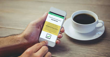 Composition of man holding smartphone with covid 19 international certificate of vaccination. global...