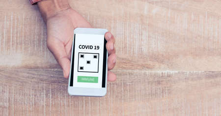 Composition of man holding smartphone with covid 19 application. global coronavirus pandemic, health and covid 19 passport concept digitally generated image.の写真素材