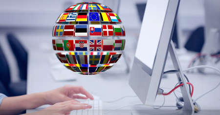 Composition of globe of world flags over midsection of woman using computer at desk in office. global communication and business technology concept digitally generated image.の写真素材