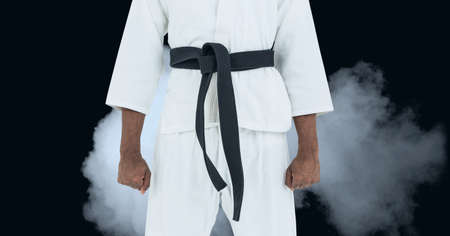 Composition of midsection of male martial artist with black belt over clouds of smoke. sports and...