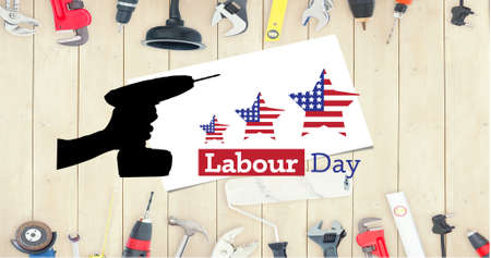 Silhouette of hand holding tool and happy labor day text against multiple tools on wooden...
