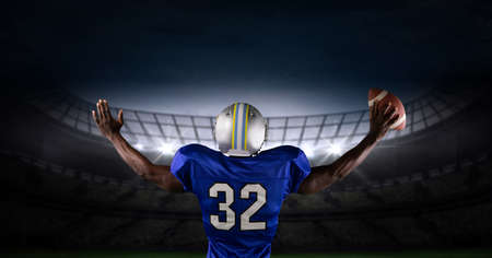 Rear view of african american male rugby player wearing helmet holding a rugby ball against stadium....