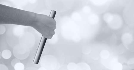 Black and white image of close up of hand holding a baton against spots of bokeh light in...