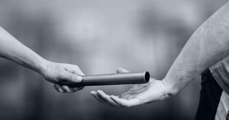 Black and white image of close up of hand passing a baton against grey background. sports and fitness conceptの写真素材