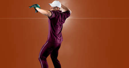 Caucasian male baseball pitcher throwing the ball against spot of light on orange background. sports...