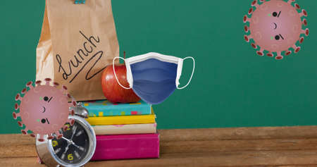 Composition of angry faced covid viruses and face mask over apple, schoolbooks and lunch bag....
