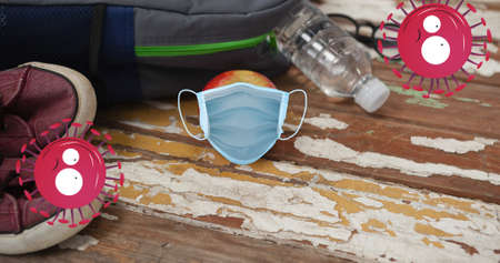 Composition of angry faced covid viruses and face mask over apple, schoolbag and shoes on floor. school, education and study during covid 19 pandemic concept digitally generated image.の写真素材