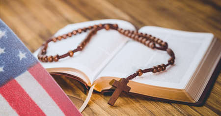 Waving american flag against cross over bible on wooden background. american patriotism and religion...
