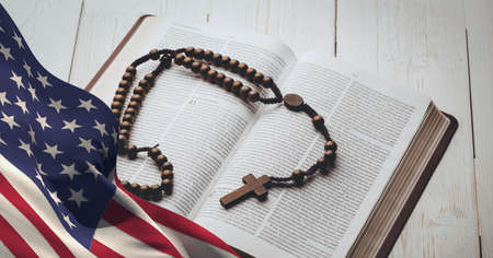 Waving american flag against cross over bible on wooden background. american patriotism and religion...