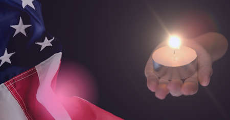 Composition of hands holding lit tea light candle and american flag billowing on dark background. patriotism, independence and celebration concept digitally generated image.の写真素材