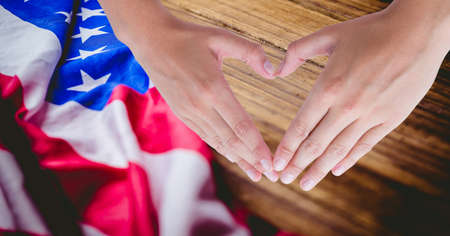 Composition of hands making heart shape with american flag on wood background. patriotism, independence and celebration concept digitally generated image.の写真素材