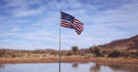 Composition of american flag on flagpole billowing over lake, landscape and blue cloudy sky. patriotism, independence and celebration concept digitally generated image.の写真素材