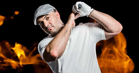 Portrait of caucasian male golf player swinging club against fire flame effect on black background....