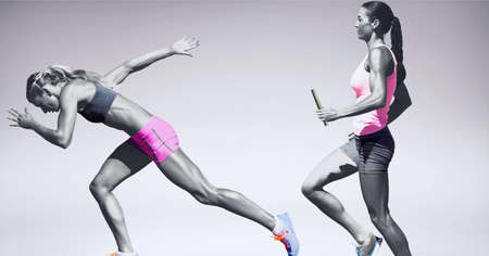 Two diverse female athletes holding baton running against grey background. sports competition and tournament conceptの写真素材