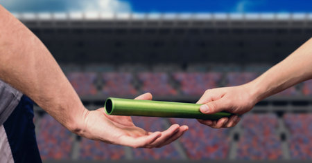 Mid section of hand passing a baton against sports stadium in background. sports competition and tournament conceptの写真素材