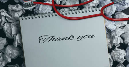 Thank you text and stethoscope over diary against crumbled paper balls in background. healthcare...
