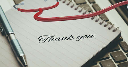Thank you text and a pen over diary and stethoscope against laptop keyboard in background. healthcare love and support conceptの写真素材