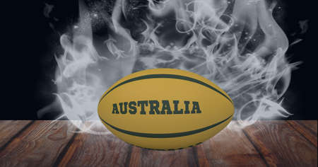 Yellow rugby ball with australia text over wooden surface against smoke effect on black background. sports tournament and competition conceptの写真素材