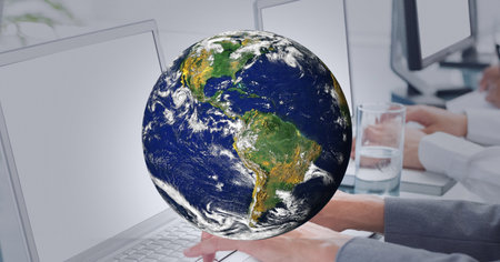 Globe against mid section of people using laptop at office. global business and technology conceptの写真素材