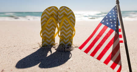 Composition of american flag and flip flops on beach. united states of america celebration, holiday, patriotism and independence concept digitally generated image.の写真素材