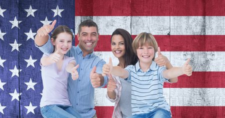Composition of smiling caucasian couple with son and daughter giving thumbs up against american flag. united states of america patriotism and independence concept digitally generated image.の写真素材