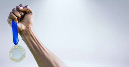 Close up of hand holding a medal against grey background. sports tournament and competition concept
