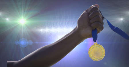 Close up of hand holding multiple medals against spots of light in background. sports tournament and...