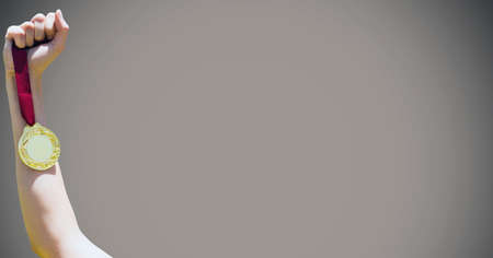 Close up of hand holding a medal against grey background. sports tournament and competition concept