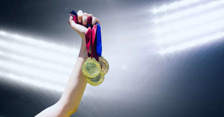 Close up of hand holding multiple medals against flood lights on black background. sports tournament and competition conceptの写真素材