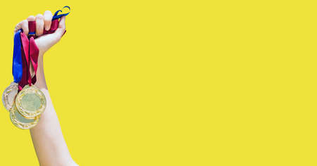 Close up of hand holding multiple medals against yellow background. sports tournament and...