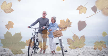 Digital composite image of multiple leaves against senior couple walking with bicycle at the beach....