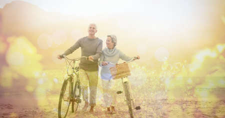 Digital composite image of spots of light against senior couple walking with bicycle at the beach. retirement senior couple lifestyle living conceptの写真素材