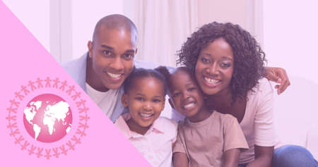 Composition of pink globe icon, with smiling family indoors. breast cancer positive awareness campaign concept digitally generated image.の写真素材