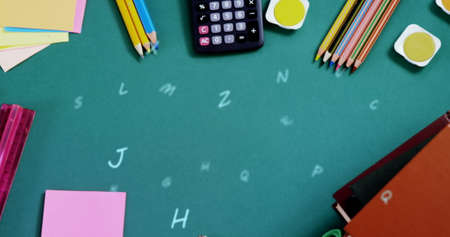 Digital composition of multiple alphabets floating against school stationary equipment on green surface. school and education conceptの写真素材