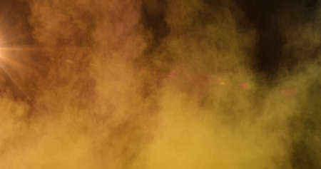 Image of orange and yellow coloured powder bomb with clouds of smoke and glowing spot of light in the background. Colour light movement concept digitally generated image.の写真素材