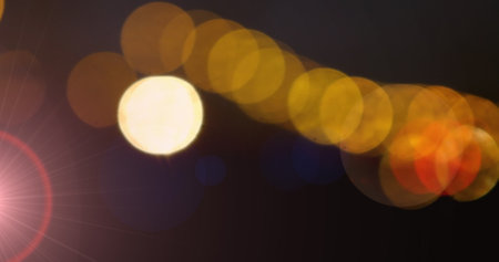 Image of a line of glowing yellow and orange spots of bokeh light moving on a dark background with lens flare. Light, colour and movement concept digitally generated image.の写真素材