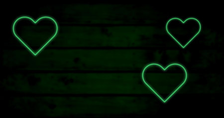Image of three green neon heart flashing on dark wood background. valentines day, love and romance concept, digitally generated image.の写真素材