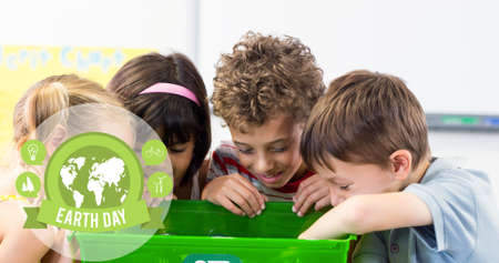 Composition of green globe logo and earth day text over children looking in recycling box. global...